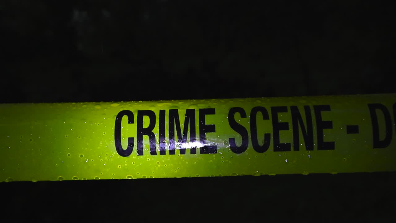 Close up of yellow crime scene tape in a dark forest during a rainy night, illuminated by side lighting as raindrops flow across the surface, creating a moody cinematic atmosphere
