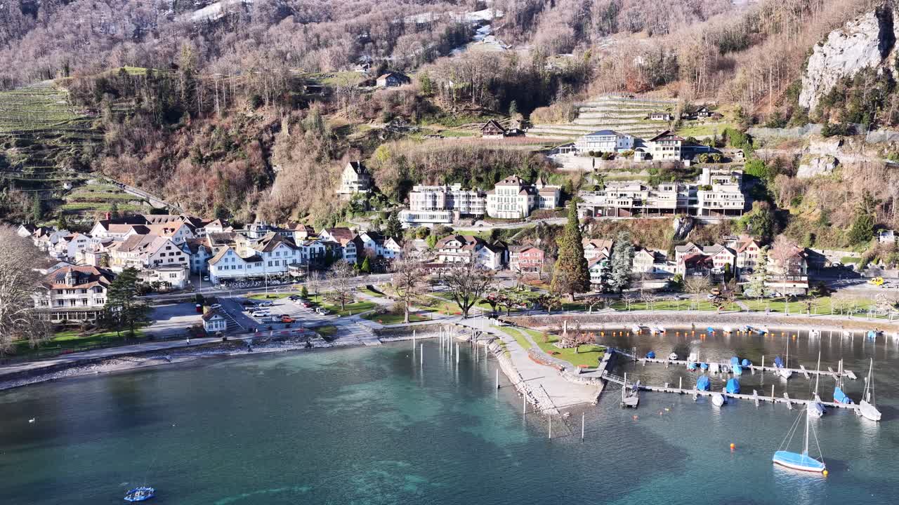 Aerial view of a peaceful Swiss lakeside village by Walensee, showing houses, marina and calm blue water on a clear day