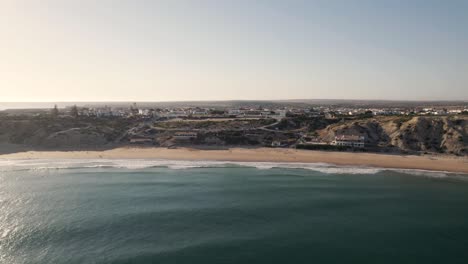 Aerial-flying-forward-Sandy-bay-protected-by-rocky-cliffs,-Mareta-Beach---Sagres