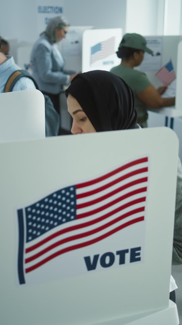 Arabic woman in hijab votes in booth in polling station office. National Election Day in United States. Political races of US presidential candidates. Concept of civic duty and patriotism. Dolly shot.