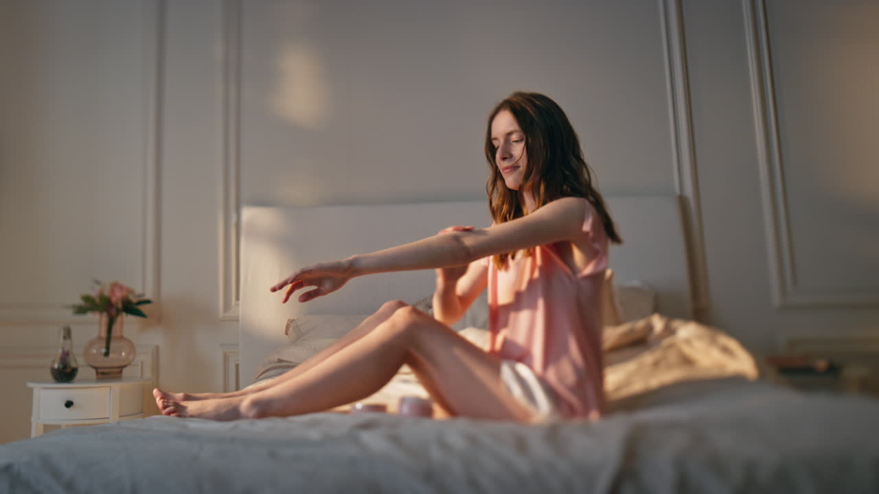 Donna che applica crema sul corpo alla luce dorata del sole. Ragazza felice e rilassata che si gode il momento.