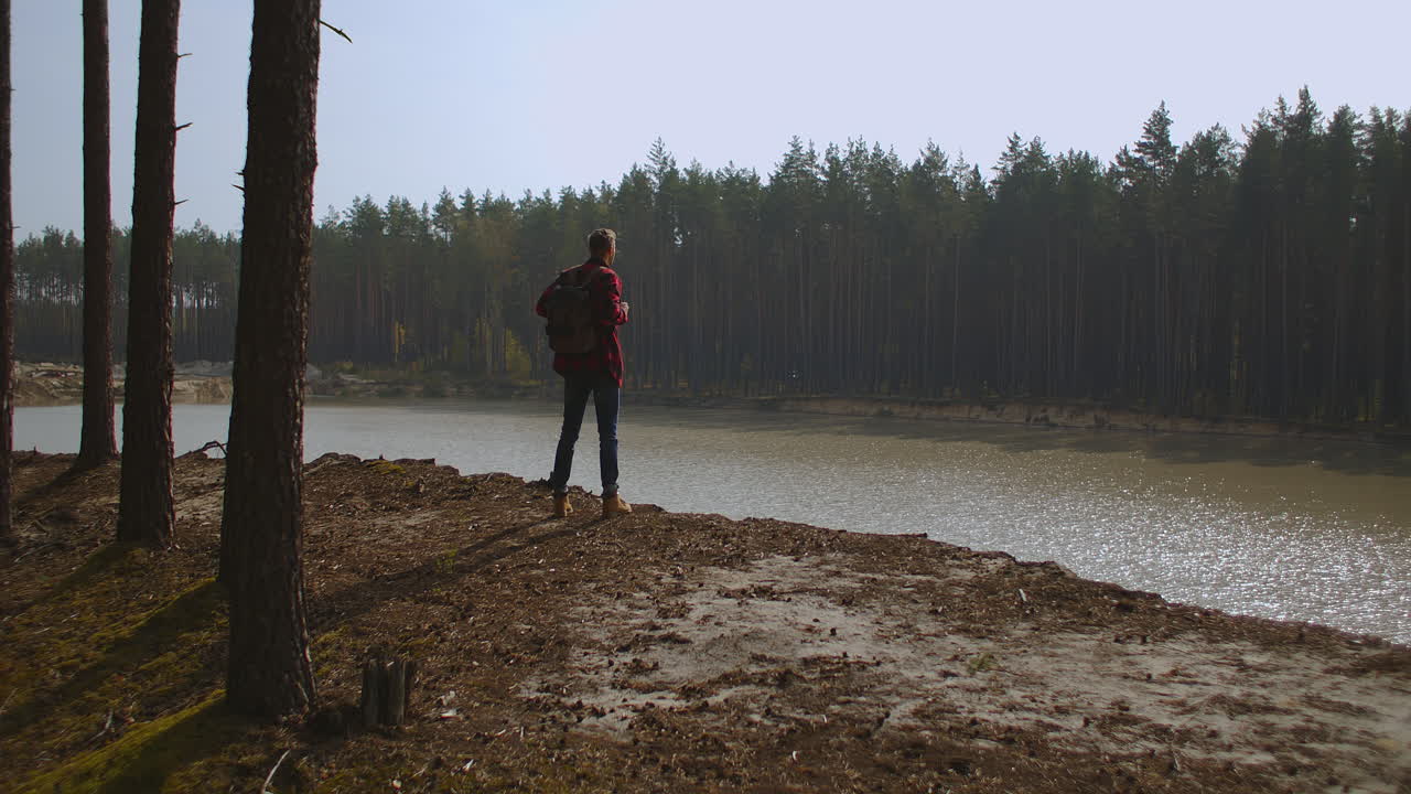 un hombre camina por un sendero en un parque cerca de un lago a primera hora de la mañana en el otoño. hombre en la cima de la colina. joven de pie en el muelle con los brazos extendidos. imágenes de alta calidad 4k
