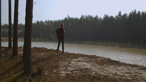 A-man-walks-along-a-path-in-a-park-near-a-lake-in-the-early-morning-in-the-autumn.-Man-Hill-Top.-Young-Man-Standing-On-Pier-With-Arms-Outstretched.-High-quality-4k-footage