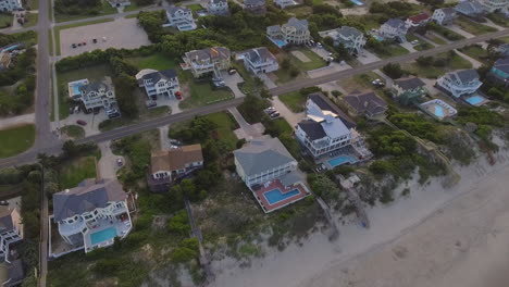 Revealing-drone-shot-of-the-sun-setting-behind-beach-houses-on-the-coast-on-the-outer-banks-of-North-Carolina