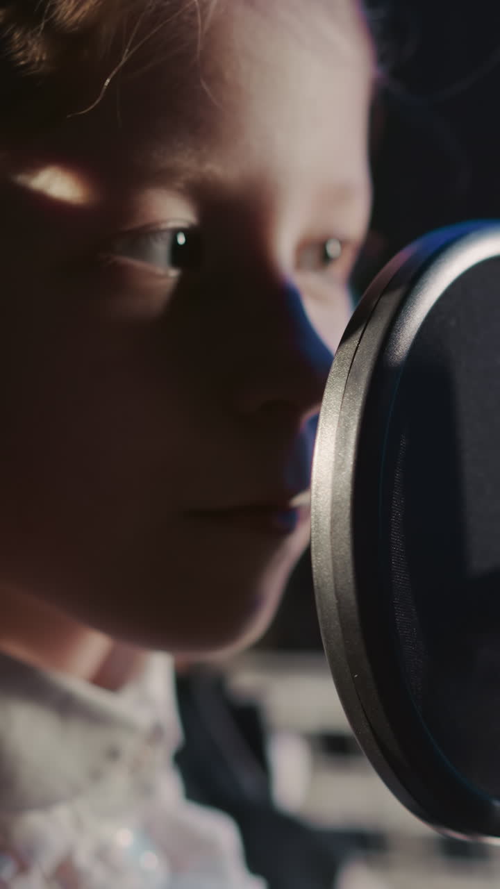 un niño toca el micrófono en un estudio de grabación. una joven inquisitiva con auriculares inspecciona el micrón con el dedo en una habitación acústicamente aislada.