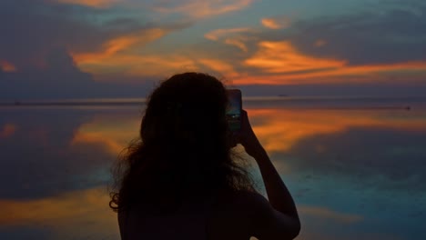 woman taking a photo of a beautiful sunset over the ocean
