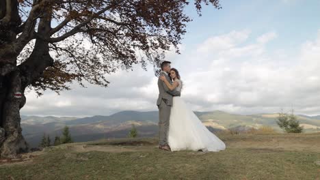 Lovely-young-newlyweds-bride-groom-embracing-on-mountain-autumn-slope,-wedding-couple-family-in-love