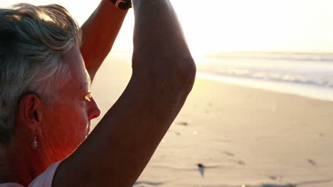 mujer mayor haciendo yoga en la playa