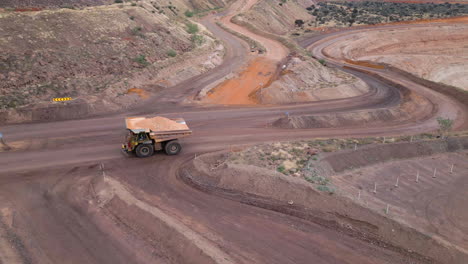 Aerial of mining dump truck full of ore material drives along a dirt road on a mine