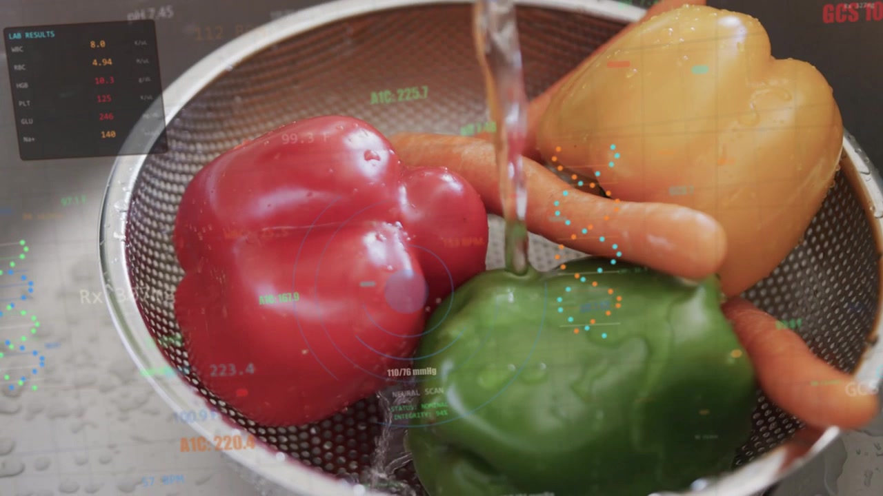 Rubinetto che eroga un getto d'acqua, scolapasta con peperoni e carote che vengono sciacquati per essere lavati, mentre un HUD traccia le gocce.