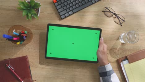 vista de arriba hacia abajo de una computadora portátil con pantalla verde simulada pantalla chromakey en un escritorio de oficina de madera al lado de la libreta con bolígrafos, gafas y un vaso de agua.