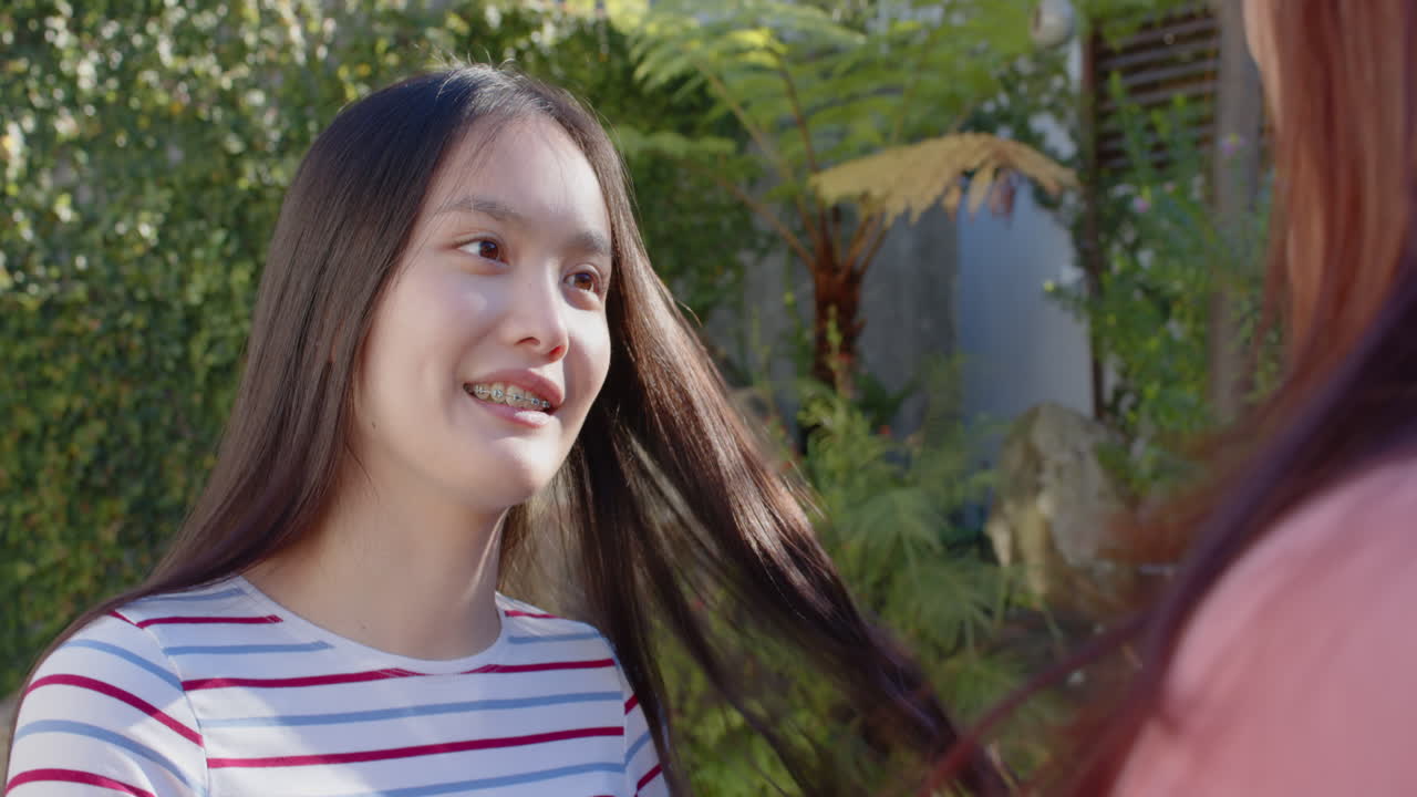 Smiling young woman with braces talking to another person outdoors