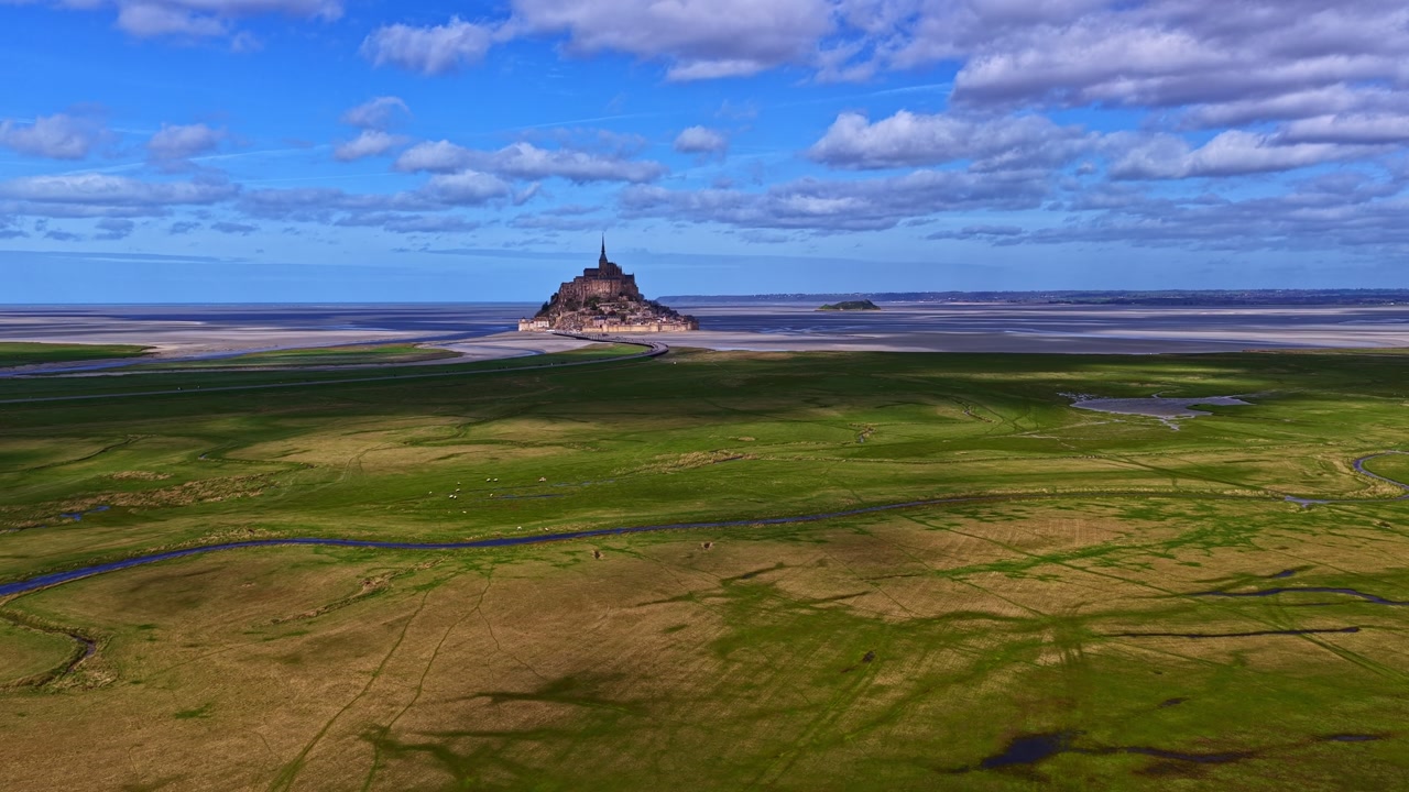 Mont Saint-Michel island fortress in France, surrounded by vast tidal area under a blue sky in aerial view