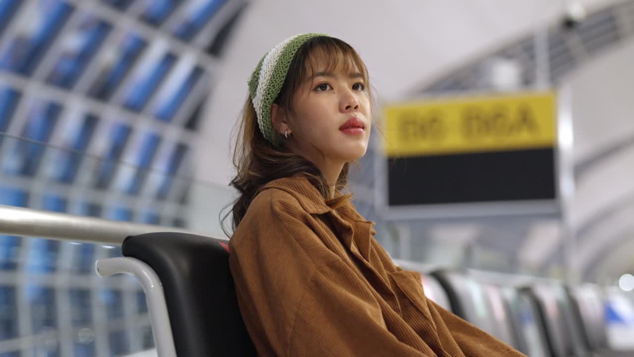 アジアの女性が空港ターミナルで乗り込みゲートで飛行機を待っている間携帯電話を使っています