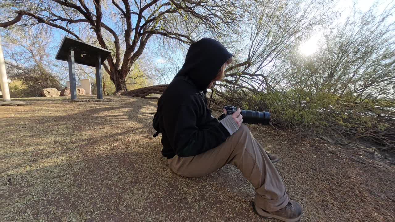 Red head man in black using a camera on the edge of a bond filming birds.