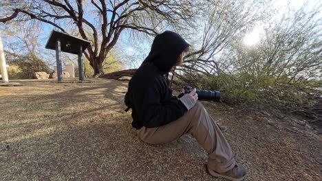 red head man in black using a camera on the edge of a bond filming birds.