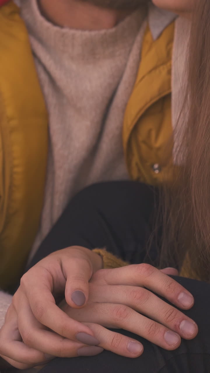 happy young couple guy and girl join hands sitting at camp bonfire on meadow at evening sunlight extreme close view