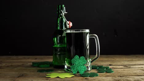 Green-beer,-bottle-and-shamrocks-on-wooden-table-for-st-patricks