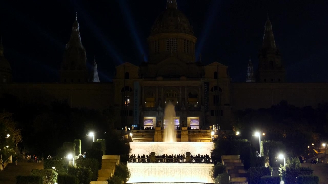 Il Museo Nazionale d'Arte della Catalogna e le fontane risplendono dopo il tramonto sopra la folla di Barcellona.