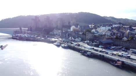 idyllic sunny conwy castle and harbour fishing town boats on coastal waterfront aerial dolly left