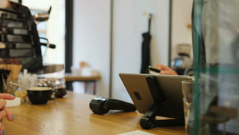 Close-up-view-of-woman-hands-paying-for-a-coffe-with-credit-card-with-help-of-barista-in-a-coffee-shop