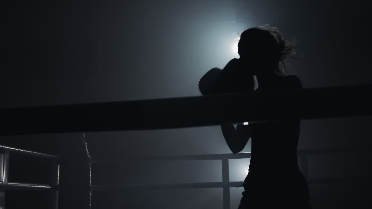 Silhouette di una pugilessa che si allena in un ring fumoso in controluce