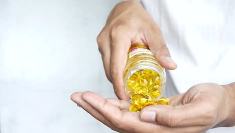 person pouring fish oil capsules from a bottle into their hand