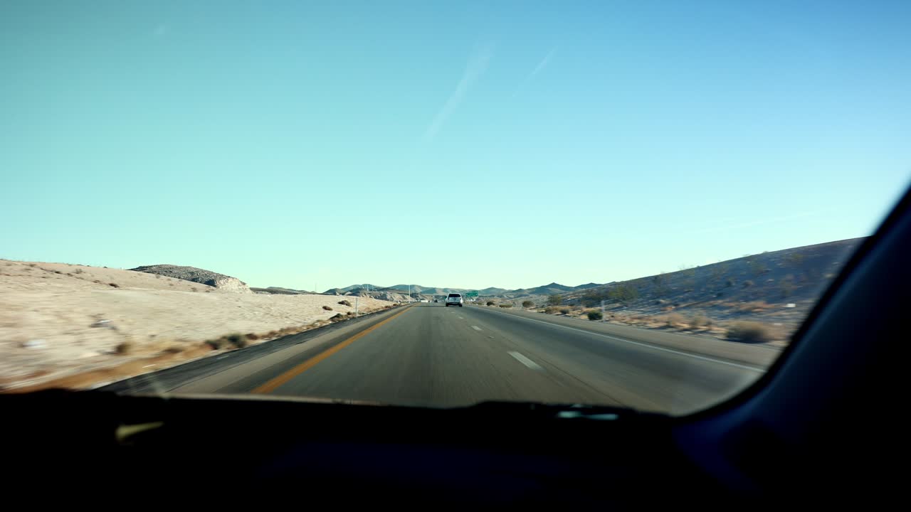 Passenger view from car riding on desert highway below cloudless sky