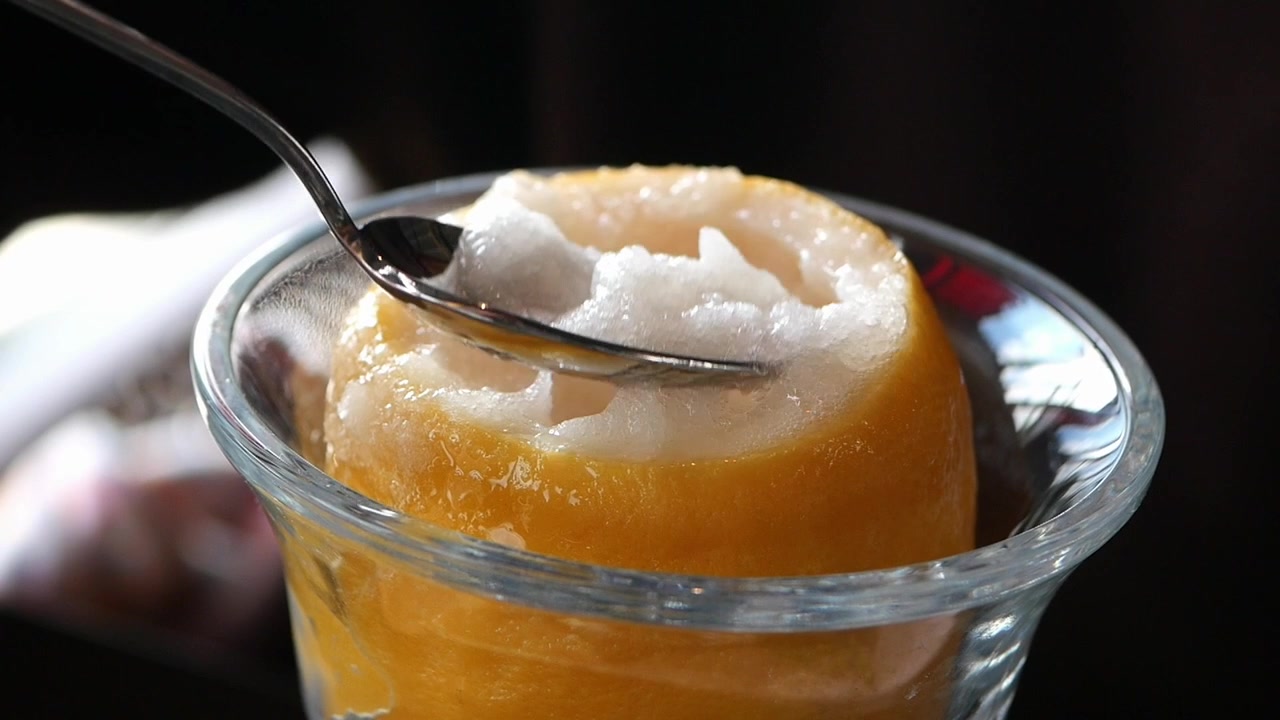 Primo piano di un cucchiaio che preleva rinfrescante sorbetto al limone da un frutto.