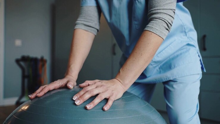 Therapist in scrubs shifting and holding stability ball in clinic after placing hands for balance