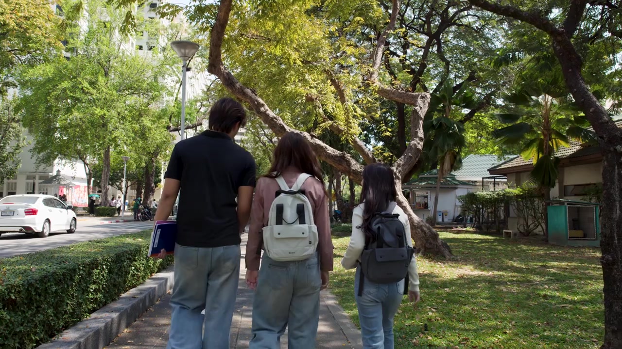Tre studenti universitari thailandesi si allontanano dalla telecamera attraverso un soleggiato parco universitario all'aperto
