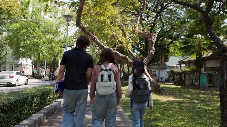 Tre studenti universitari thailandesi si allontanano dalla telecamera attraverso un soleggiato parco universitario all'aperto
