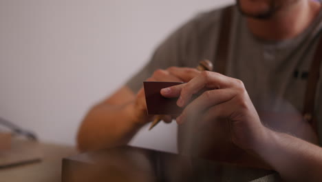 Man-applies-glue-onto-leather-details-edge-at-workplace