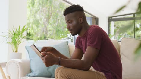 Video-of-relaxed-african-american-man-sitting-on-sofa-and-using-tablet