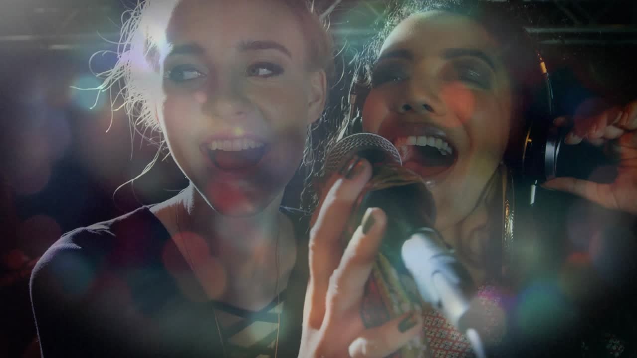 Two female singers reacting to backlight on music stage leaning into mic cupping phones harmonizing