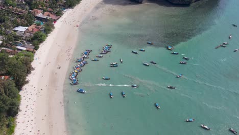 Aerial-View-Across-Beach-In-Krabi-With-Group-Of-Longtail-Boats-Moored-With-Tilt-Up-Reveal-Of-Limestone-Cliffs