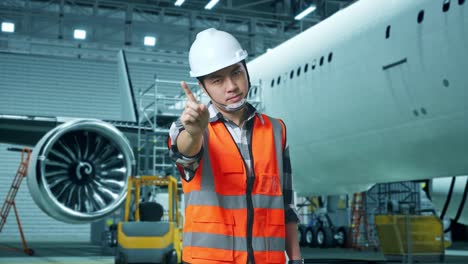 ingeniero masculino asiático con casco de seguridad desaprueba sin señal del dedo índice mientras está de pie con la aeronave en el hangar