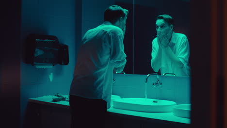 man washing face in a nighttime bathroom