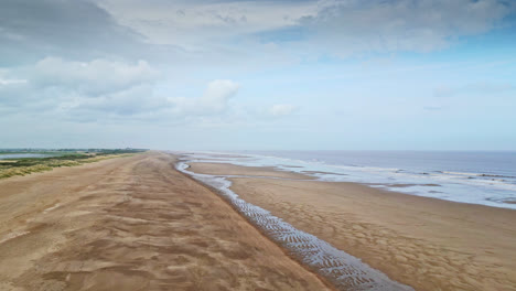 Aerial-video-footage-of-a-coastal-beach-scene-with-ocean,-sand-dunes-and-crashing-waves