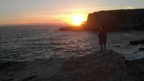 slow and dramatic footage of a sunset revealing a woman standing on a huge rock