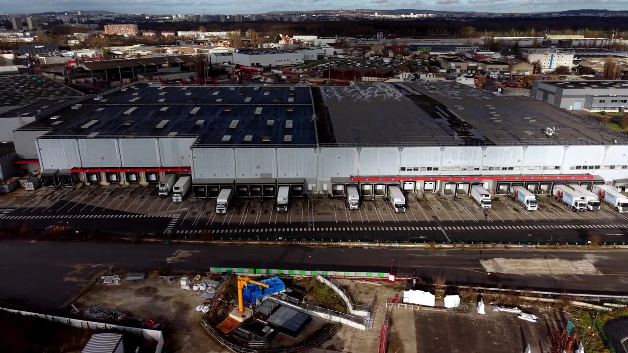 Modernes Logistikzentrum mit Lastwagen an Laderampen in einem Industriegebiet, Frankreich. Drohnenansicht.