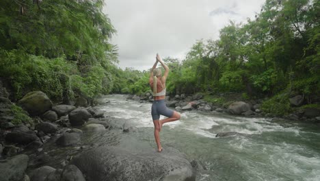 Colocar-Mujer-Caucásica-En-Ropa-Deportiva-En-Pose-De-árbol-En-Roca-Junto-Al-Río