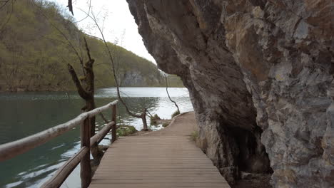 a man made wooden footpath between a clear blue lake and mountain cliff side