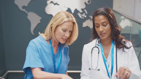 female doctors in white coat and scrubs discussing patient notes in informal meeting in hospital