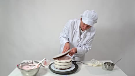 a baker woman, in a white robe, puts the last layer of the cake on the sugar cream. confectionery for baking.
