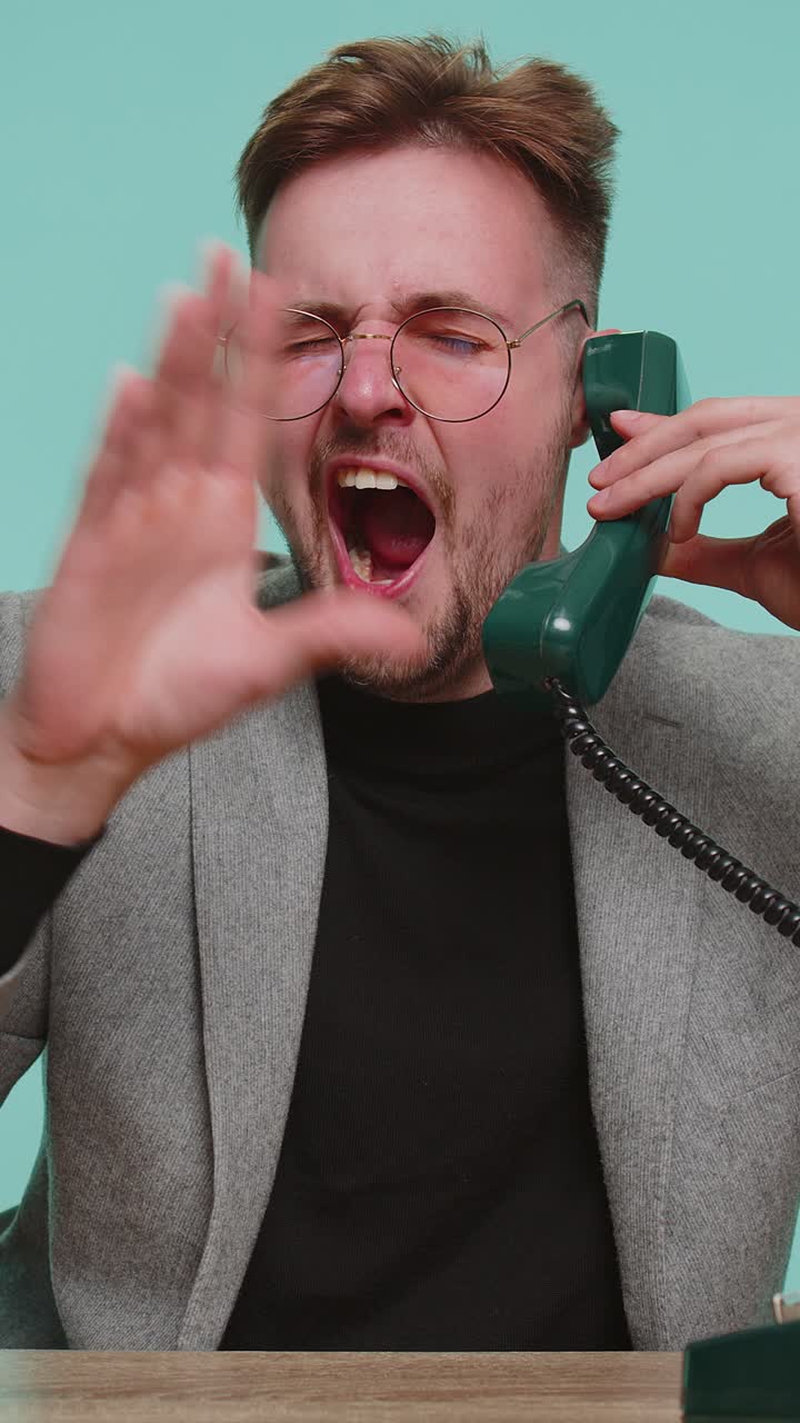 Hombre de negocios cansado y aburrido hablando por un teléfono fijo vintage de los 90, haciendo el tonto y poniendo caras graciosas