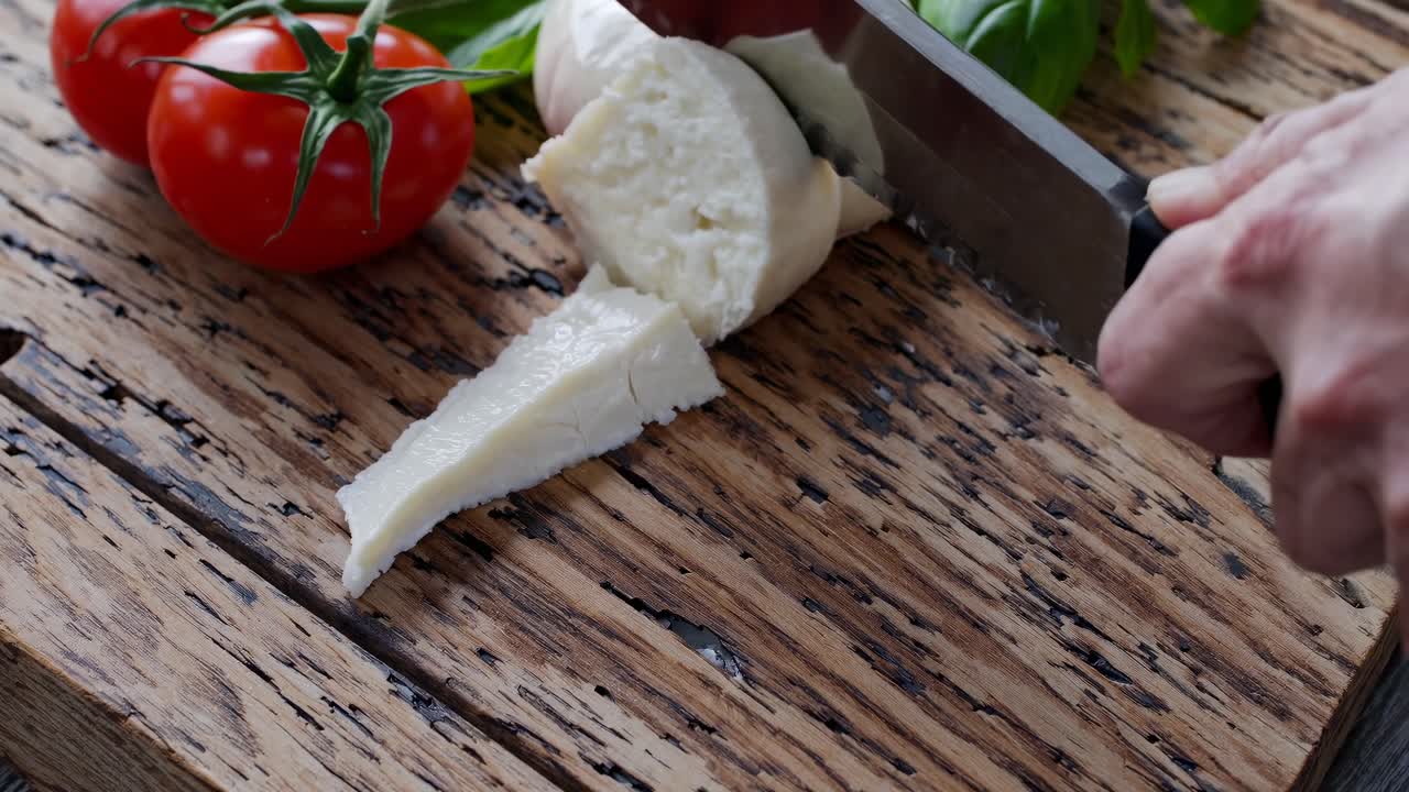 Close-up video shot of fresh mozzarella on rustic wood, surrounded by basil and tomatoes