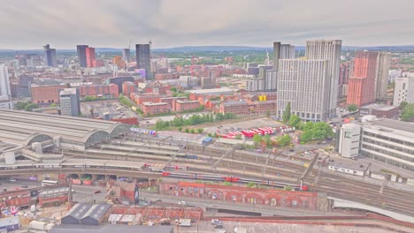 wide-angle aerial static shot of manchester city centre showing the train station, modern high-rises, and industrial heritage structures with cloudy sky and urban infrastructure in the foreground