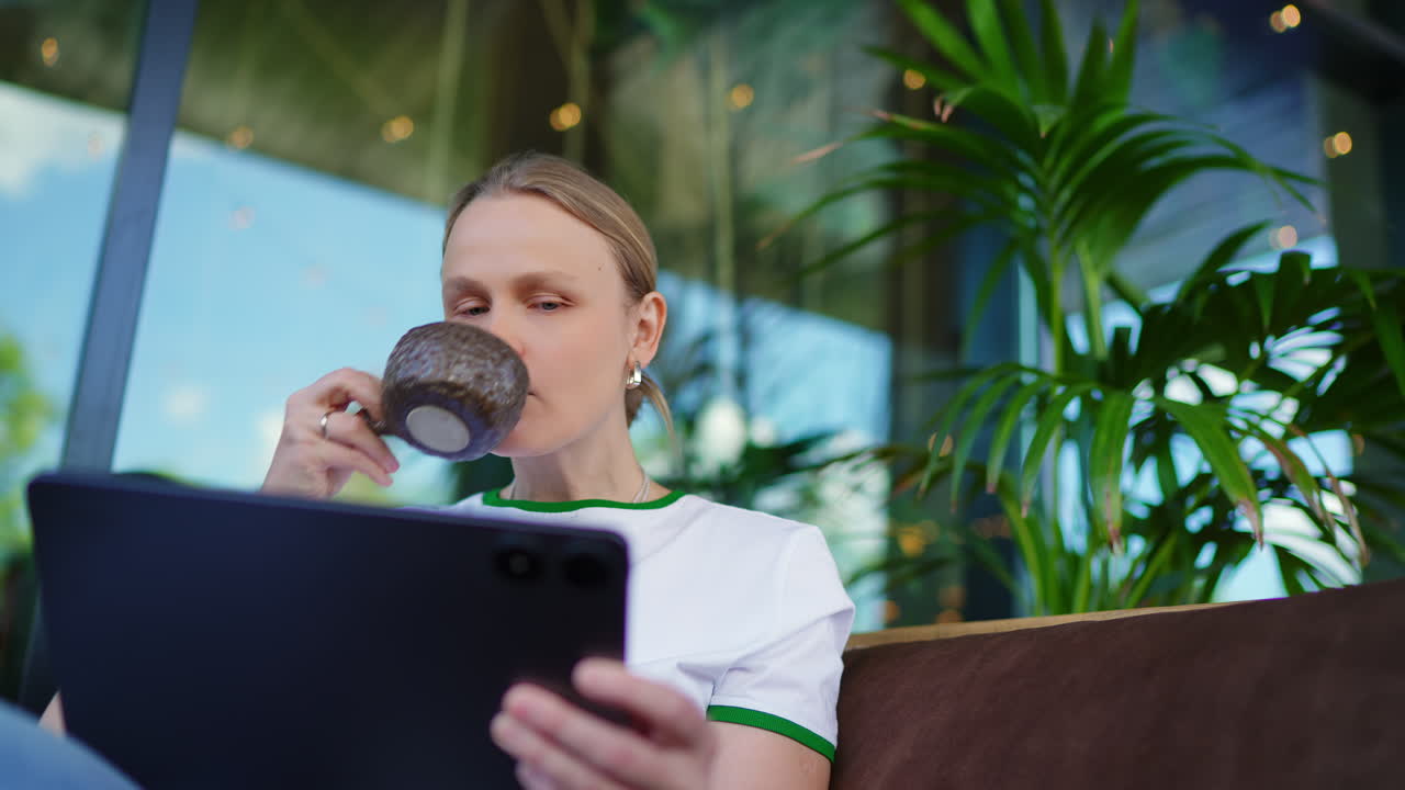 Giovane Donna che Usa il Tablet e Beve Caffè in un Caffè Moderno