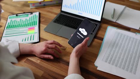 person using a smartphone for cloud data upload amidst business documents and laptop
